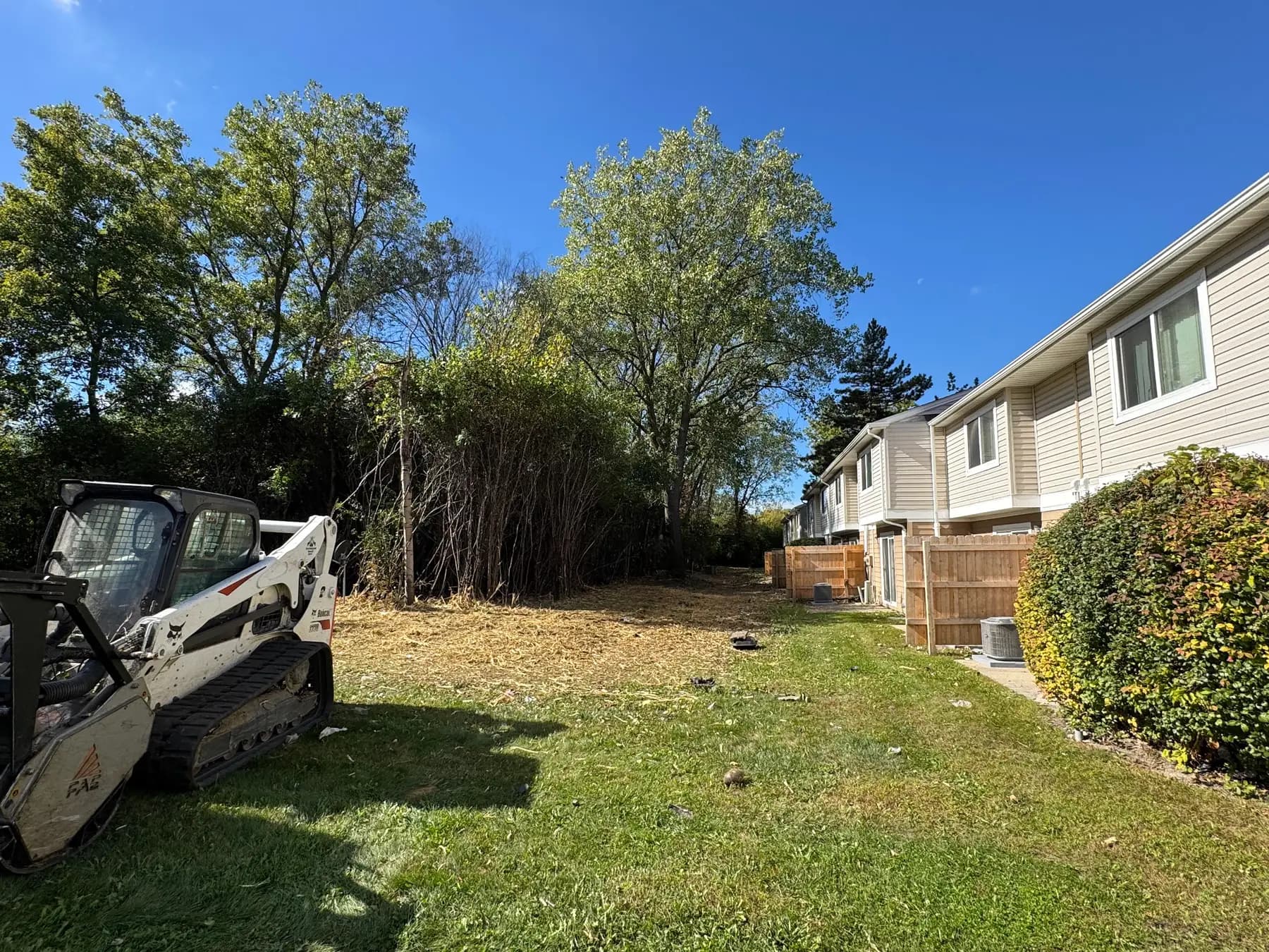 Bobcat forestry mulcher clearing overgrown brush behind an apartment complex