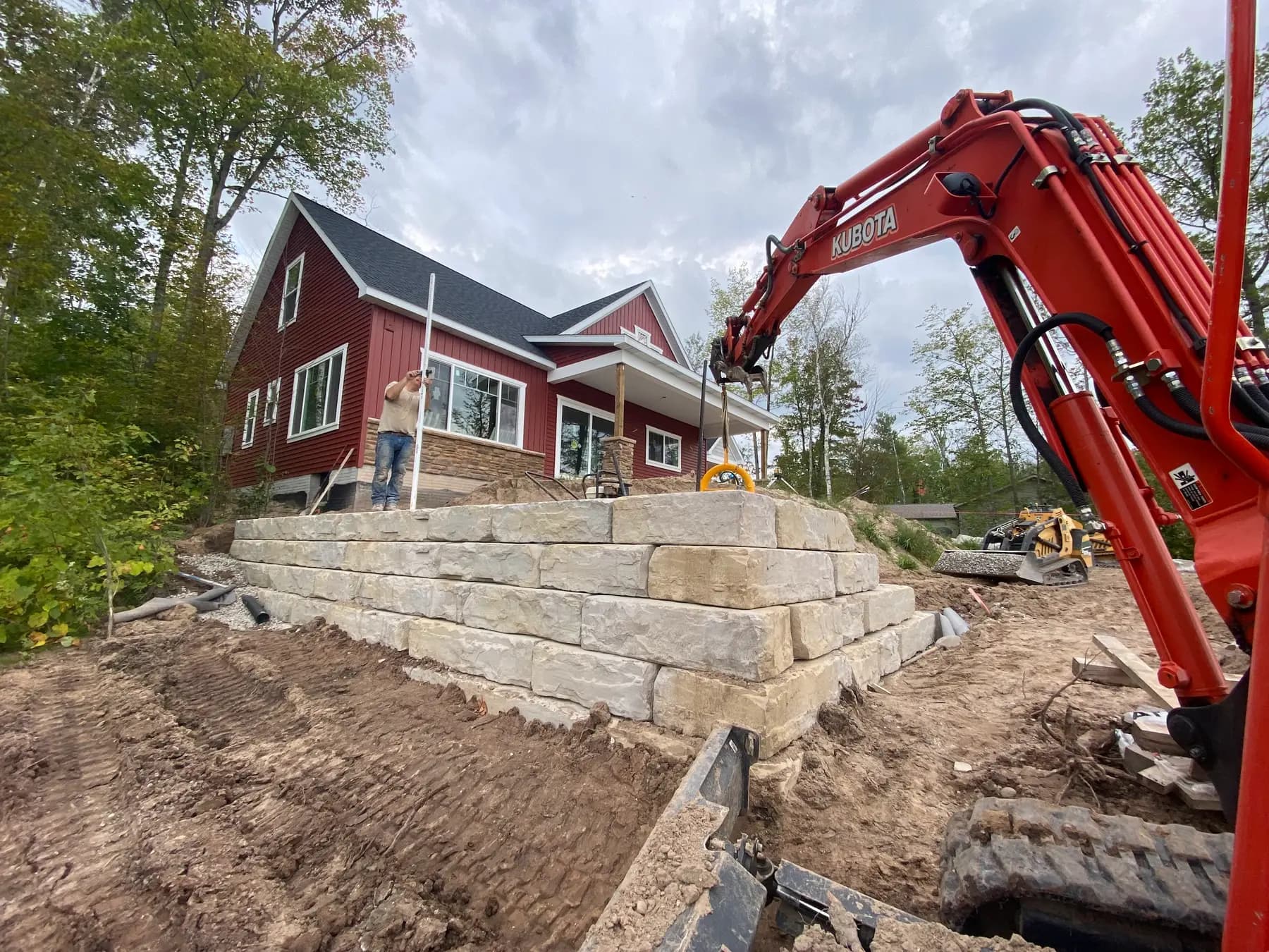 Excavator setting large block for a retaining wall beside a new home